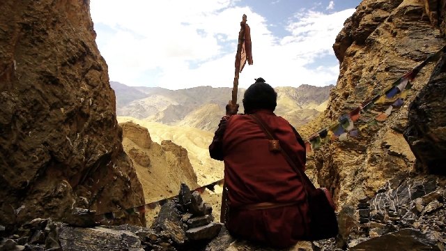 Das Bild zeigt einen tibetischen Pilger, der auf die sich vor ihm ausbreitende Berglandschaft guckt.